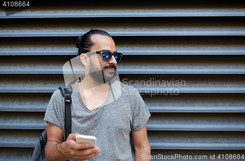 Image of man with backpack texting on smartphone in city
