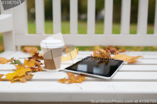 Image of tablet pc and coffee cup on bench in autumn park