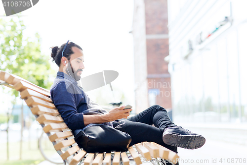 Image of man with earphones and smartphone on city bench