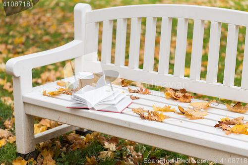 Image of open book and coffee cup on bench in autumn park