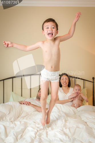 Image of Mixed Race Chinese and Caucasian Boy Jumping In Bed with His Fam