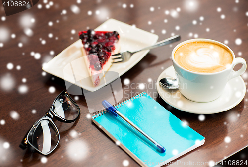 Image of close up of notebook with pen, coffee cup and cake