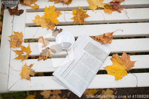 Image of newspaper and coffee cup on bench in autumn park