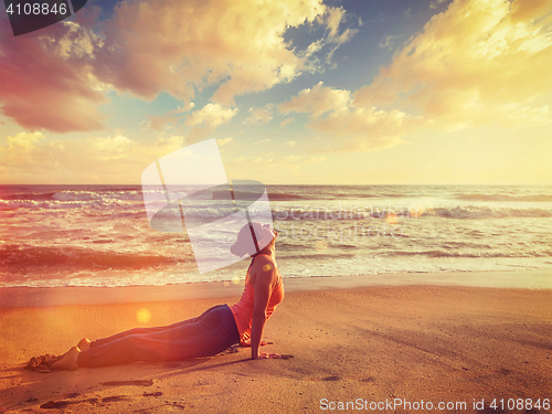 Image of Woman practices yoga asana Urdhva Mukha Svanasana at the beach