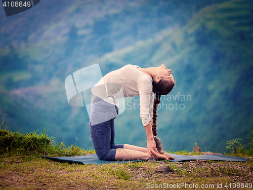 Image of Woman doing yoga asana Ustrasana camel pose outdoors