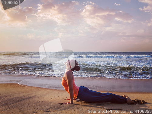 Image of Woman practices yoga asana Urdhva Mukha Svanasana at the beach