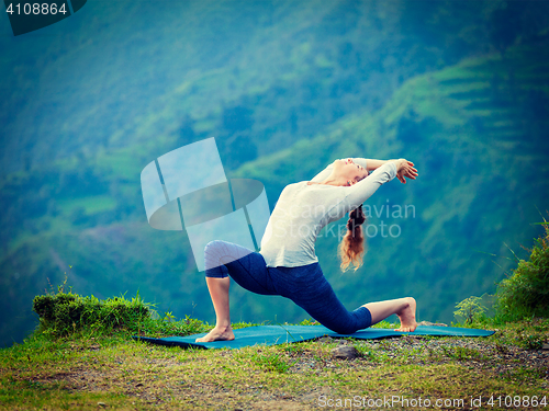 Image of Sporty fit woman practices yoga asana Anjaneyasana in mountains