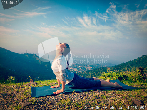 Image of Woman practices yoga asana Urdhva Mukha Svanasana outdoors