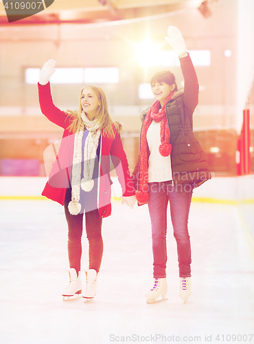 Image of happy girls friends waving hands on skating rink