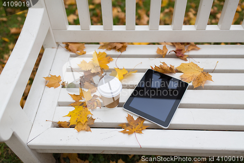 Image of tablet pc and coffee cup on bench in autumn park