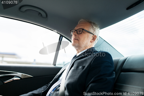 Image of senior businessman driving on car back seat