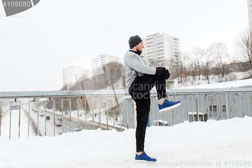 Image of man exercising and stretching leg on winter bridge