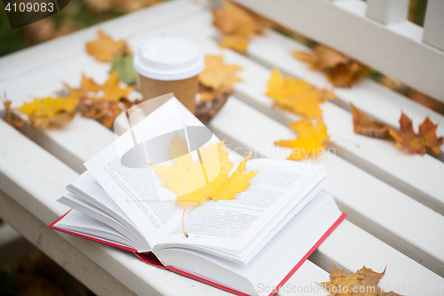 Image of open book and coffee cup on bench in autumn park