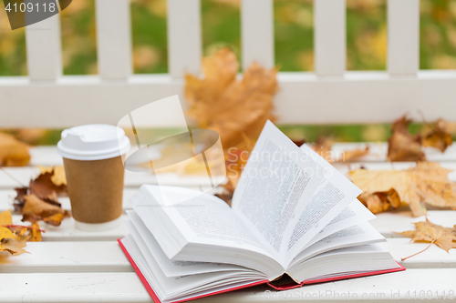 Image of open book and coffee cup on bench in autumn park