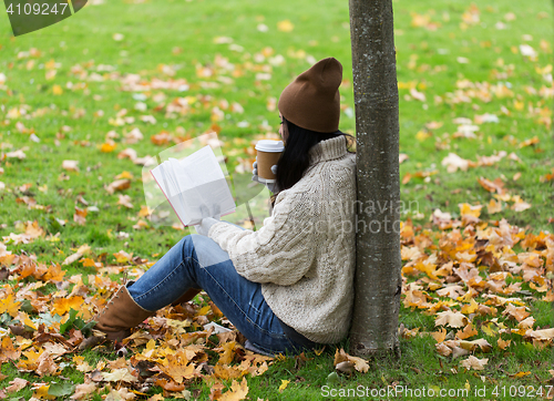 Image of woman with book drinking coffee in autumn park