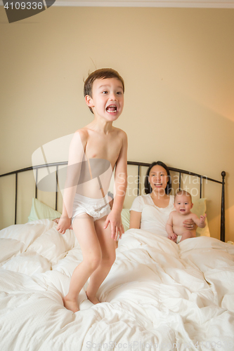 Image of Mixed Race Chinese and Caucasian Boy Jumping In Bed with His Fam