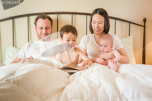 Image of Chinese and Caucasian Baby Boys Reading a Book In Bed with Their