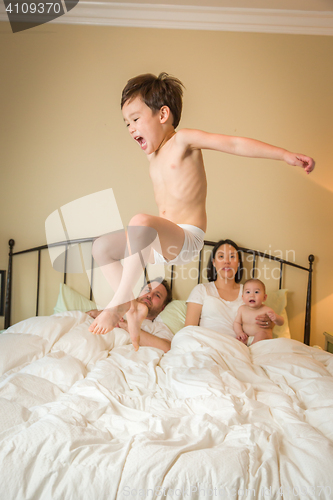 Image of Mixed Race Chinese and Caucasian Boy Jumping In Bed with His Fam