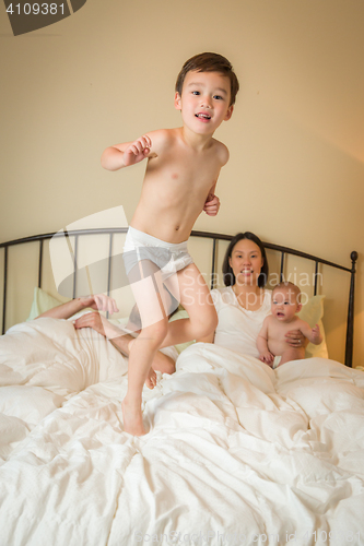 Image of Mixed Race Chinese and Caucasian Boy Jumping In Bed with His Fam