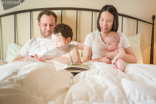 Image of Chinese and Caucasian Baby Boys Reading a Book In Bed with Their