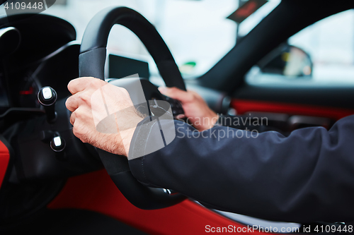 Image of Male driver hands holding steering wheel.