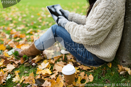 Image of woman with tablet pc and coffee in autumn park