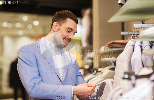 Image of happy young man choosing clothes in clothing store