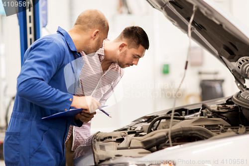 Image of auto mechanic with clipboard and man at car shop