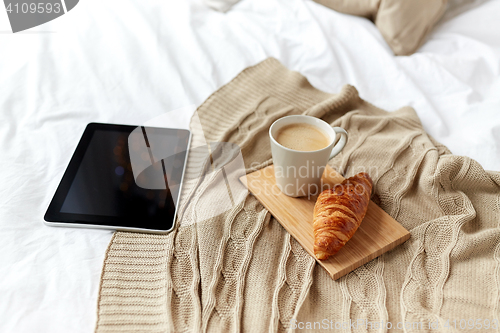 Image of tablet pc, coffee and croissant on bed at home