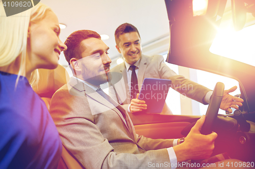 Image of happy couple with car dealer in auto show or salon