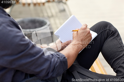 Image of close up of man writing to notebook on city street