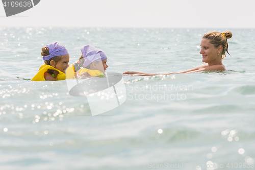 Image of Mom floats in the sea with two small daughters in swimming vests