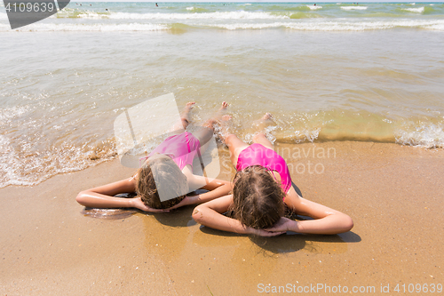 Image of Two girls lie on your back on the sandy beach and looking at sea