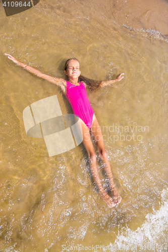 Image of Seven-year girl lies on her back in the water on the sandy beach