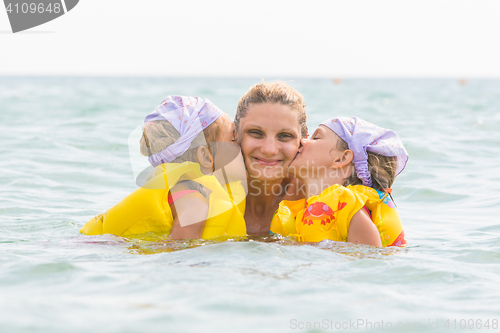 Image of Daughters kiss mom swimming in the sea