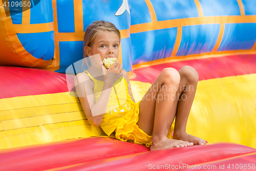 Image of Girl sits at the entrance to an inflatable trampoline and eating an apple