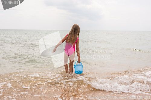 Image of Five-year girl picking up a bucket of water in the sea