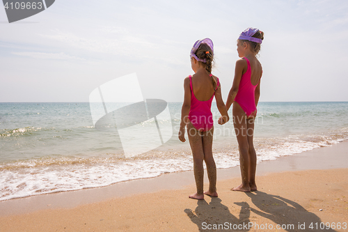 Image of Two girls in bathing suits standing on the beach and look at the horizon