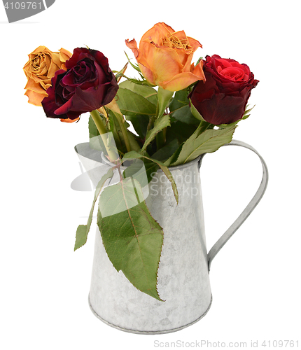 Image of Four faded rose flowers in a metal jug