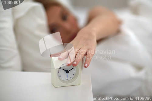 Image of close up of woman with alarm clock in bed at home