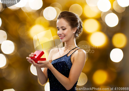 Image of smiling woman holding red gift box over lights