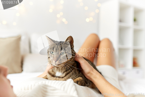 Image of happy young woman with cat lying in bed at home