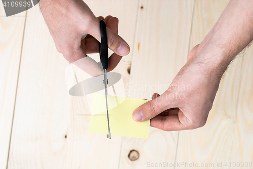 Image of hand is cutting a sheet of yellow paper