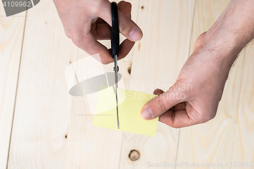 Image of hand is cutting a sheet of yellow paper