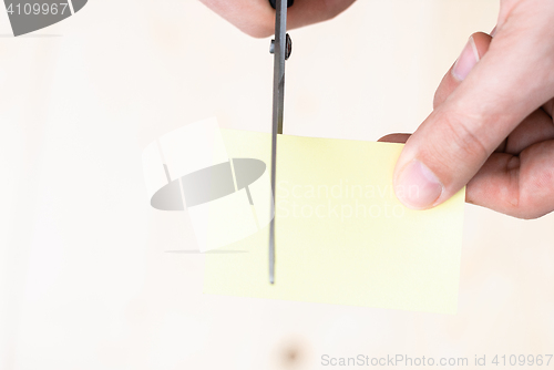 Image of A man is cutting a sheet of yellow paper using metallic scissors