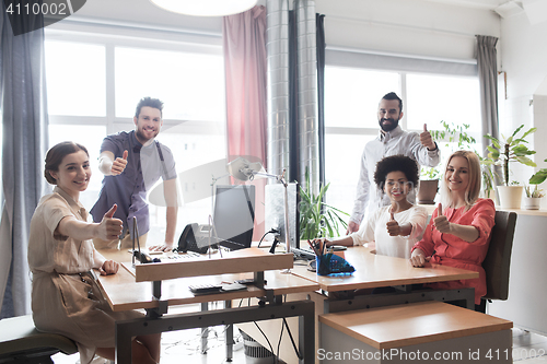 Image of happy creative team showing thumbs up in office