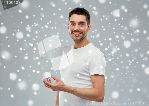 Image of happy young man with cream jar over snow