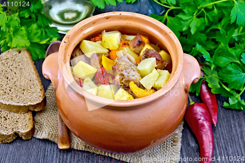 Image of Roast meat and potatoes in clay pot on dark board