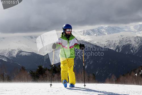 Image of Young skier with ski poles in sun mountains and gray sky before 