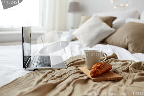 Image of laptop, coffee and croissant on bed at cozy home